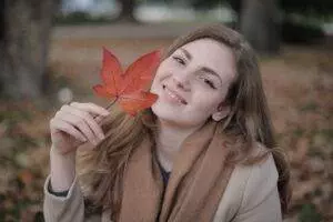 happy millennial woman with red leaf enjoying autumn in park