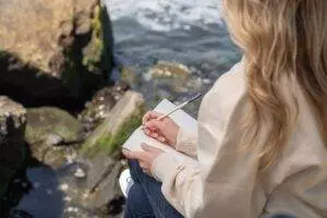 woman sitting by the water and writing in a journal