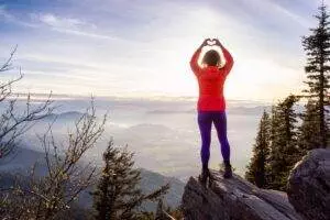 Hiking woman viewing from top of mountain with hands forming a love shape